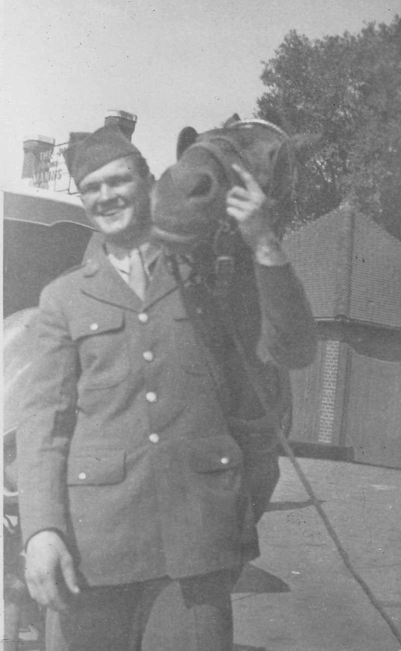 Crewman with horse in England or France. Building in background has surname Manns on signage.